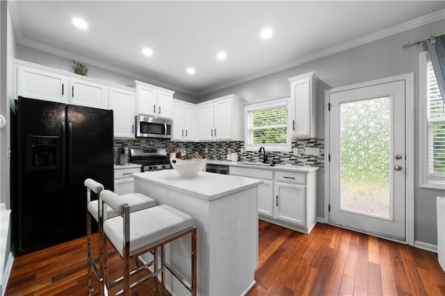 kitchen featuring stainless steel appliances, white cabinets, light countertops, a kitchen island, and crown molding