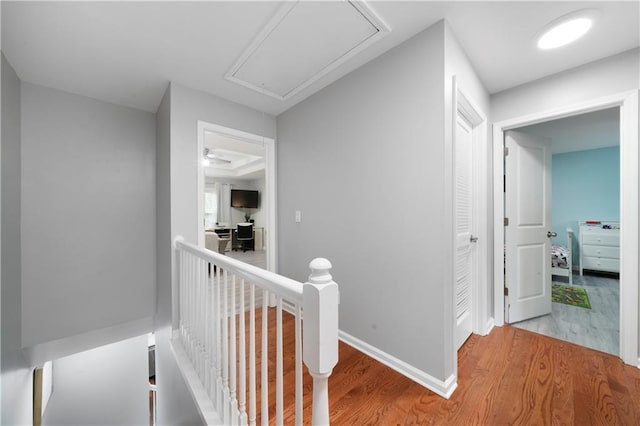 hall with attic access, wood finished floors, an upstairs landing, and baseboards
