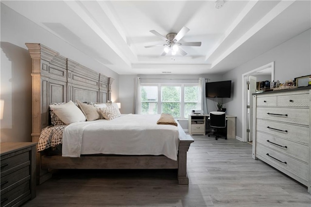 bedroom featuring a tray ceiling, light wood-type flooring, a desk, and a ceiling fan