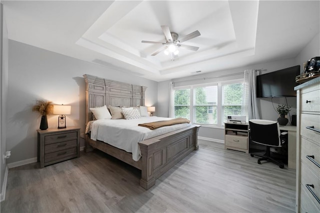 bedroom featuring a tray ceiling, light wood-style flooring, an office area, and baseboards