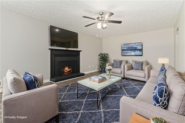 living room featuring a brick fireplace, dark hardwood / wood-style flooring, a textured ceiling, and ceiling fan