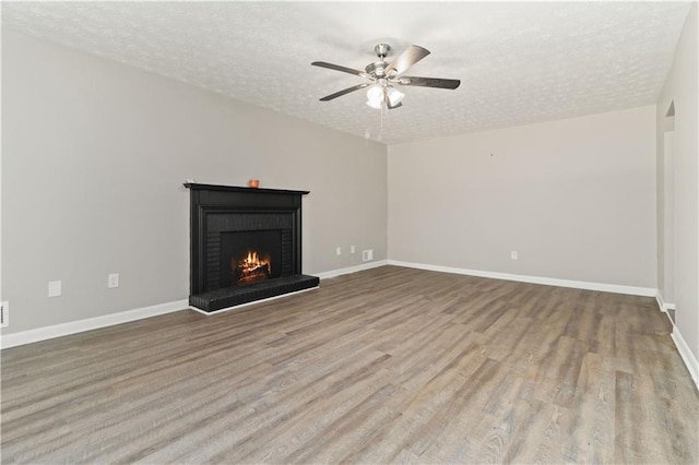 unfurnished living room with a textured ceiling, a brick fireplace, and light hardwood / wood-style flooring