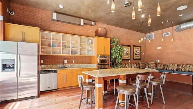 kitchen with stainless steel appliances, light wood-type flooring, brick wall, a center island, and a kitchen breakfast bar