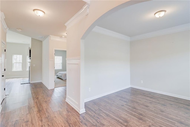 empty room featuring ornamental molding, arched walkways, baseboards, and wood finished floors