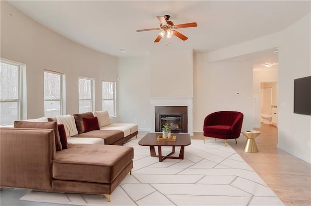 living area with light wood finished floors, baseboards, a glass covered fireplace, and a ceiling fan