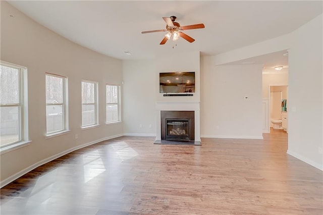 unfurnished living room with baseboards, light wood-style flooring, a glass covered fireplace, and a ceiling fan