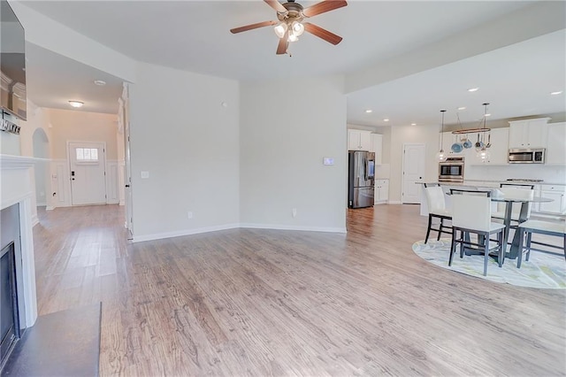 living room featuring a ceiling fan, a fireplace with flush hearth, light wood-style floors, and baseboards