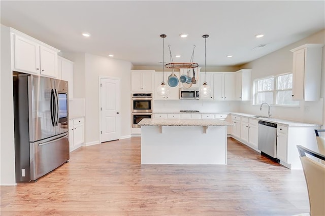 kitchen featuring a sink, a kitchen bar, appliances with stainless steel finishes, a center island, and white cabinets