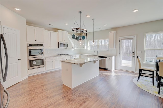 kitchen featuring white cabinetry, light wood-type flooring, a center island, a sink, and appliances with stainless steel finishes