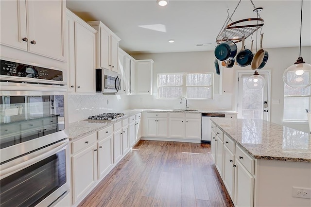kitchen with stainless steel appliances, tasteful backsplash, white cabinetry, a sink, and light wood-type flooring