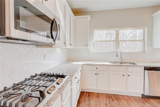 kitchen with light wood finished floors, a sink, light stone countertops, and appliances with stainless steel finishes