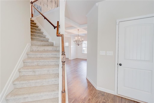 stairway with coffered ceiling, wood finished floors, beam ceiling, and a chandelier
