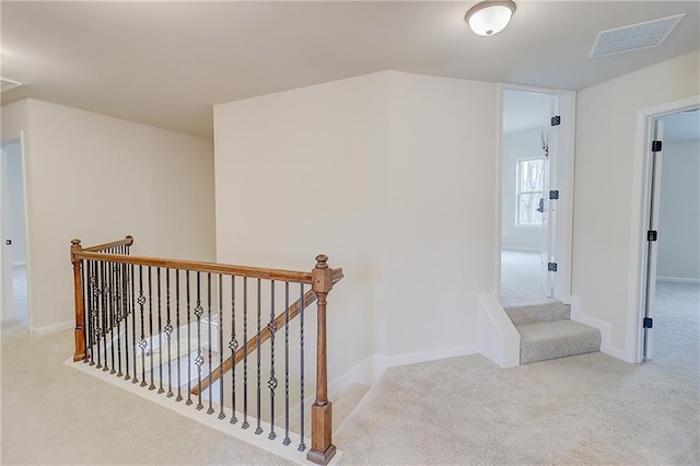 hall with baseboards, visible vents, an upstairs landing, and carpet