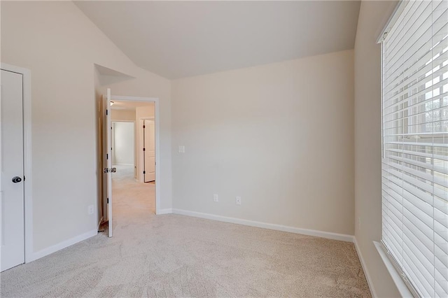 empty room featuring light colored carpet, baseboards, and vaulted ceiling
