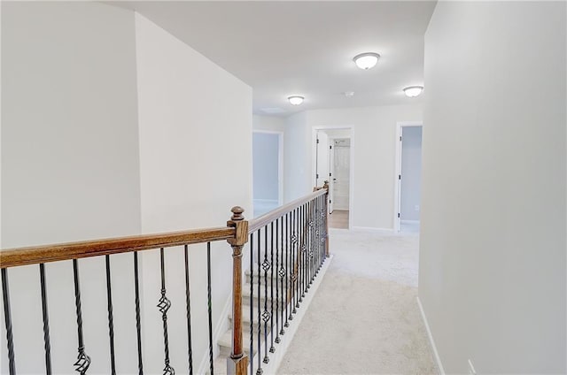 hall featuring baseboards, an upstairs landing, and light carpet
