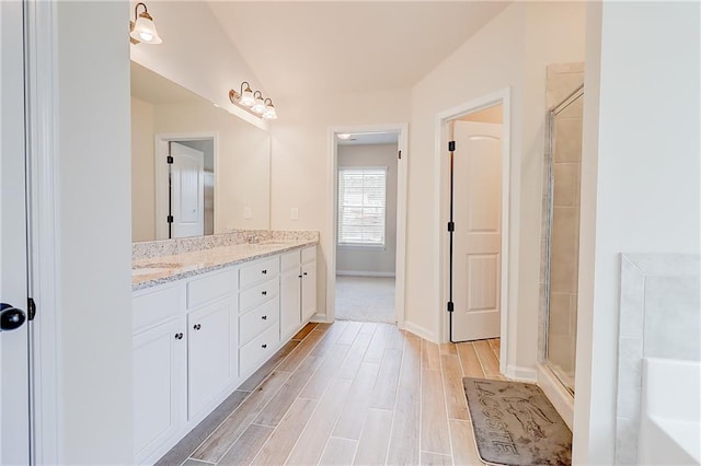 full bath with baseboards, a shower stall, a sink, double vanity, and wood finished floors