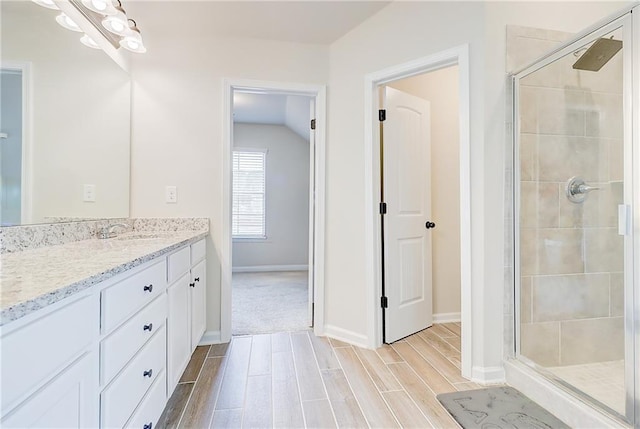 full bath featuring a stall shower, wood tiled floor, baseboards, and vanity