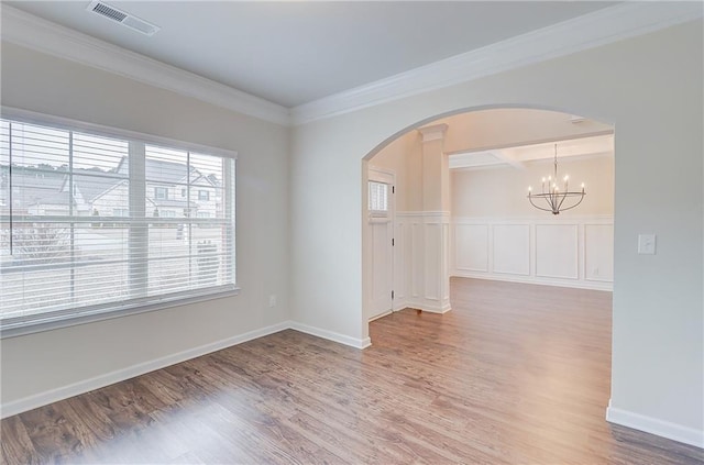 unfurnished room with an inviting chandelier, ornamental molding, arched walkways, light wood finished floors, and visible vents