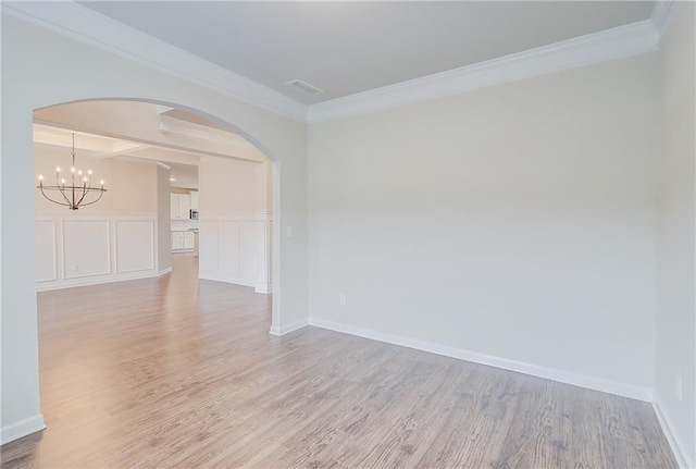 spare room with an inviting chandelier, arched walkways, crown molding, and wood finished floors