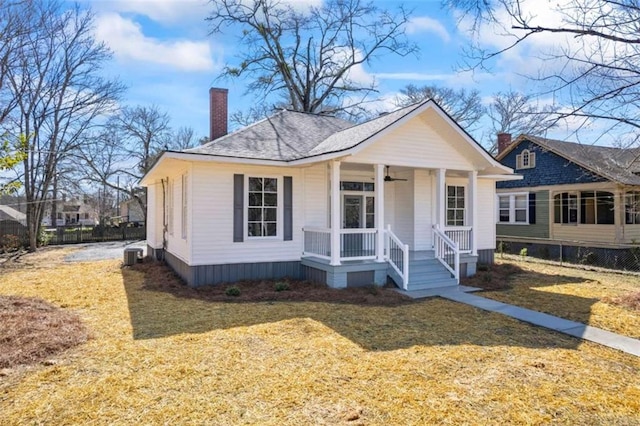 view of front of property featuring a chimney, a shingled roof, covered porch, a ceiling fan, and a front lawn