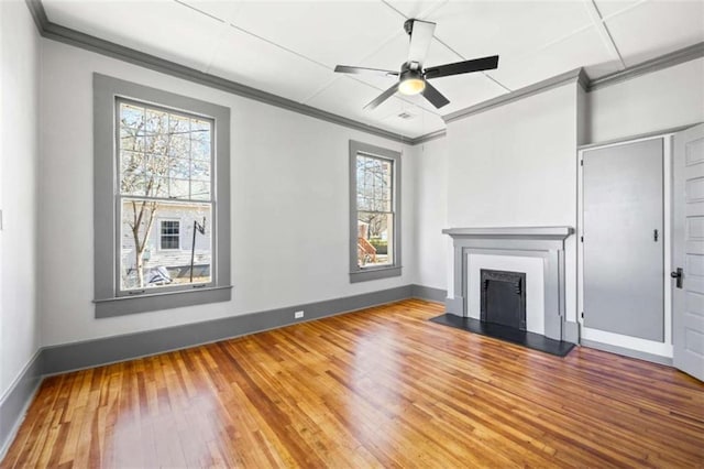 unfurnished living room with wood-type flooring, baseboards, a fireplace with raised hearth, and crown molding