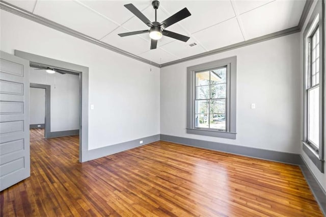 empty room featuring baseboards, visible vents, hardwood / wood-style flooring, and crown molding