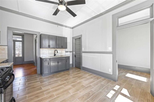 kitchen featuring wood finish floors, backsplash, gray cabinetry, stove, and a sink