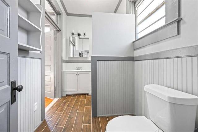 bathroom with a wainscoted wall, wood finish floors, vanity, and toilet