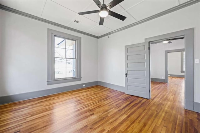 unfurnished room with visible vents, baseboards, hardwood / wood-style flooring, ceiling fan, and ornamental molding