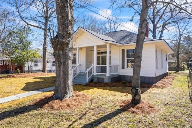 view of front of house with covered porch, ceiling fan, roof with shingles, and a front yard