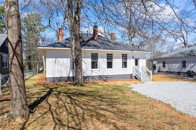 back of house with gravel driveway, a chimney, fence, and a lawn