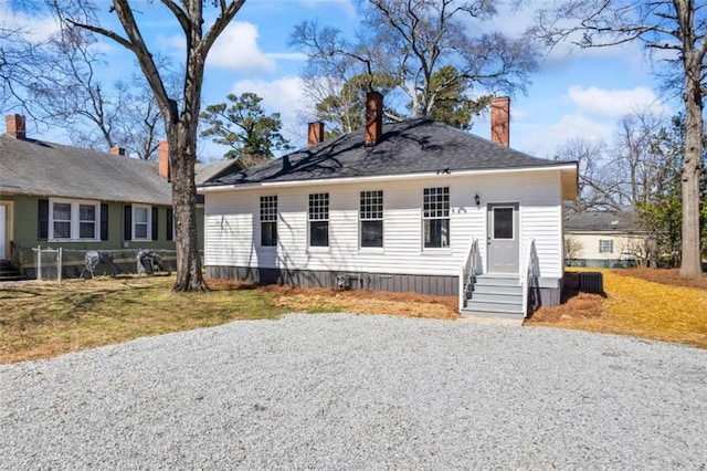 view of front of home with entry steps, driveway, a front lawn, and a chimney