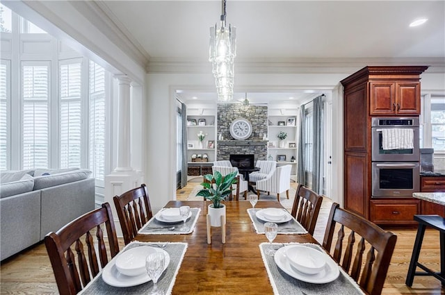 dining space featuring hardwood / wood-style floors, an inviting chandelier, crown molding, built in features, and a fireplace