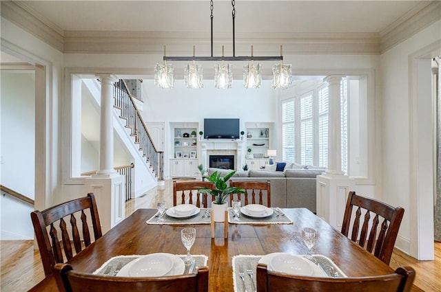 dining area featuring a notable chandelier, light wood-type flooring, crown molding, and a tiled fireplace