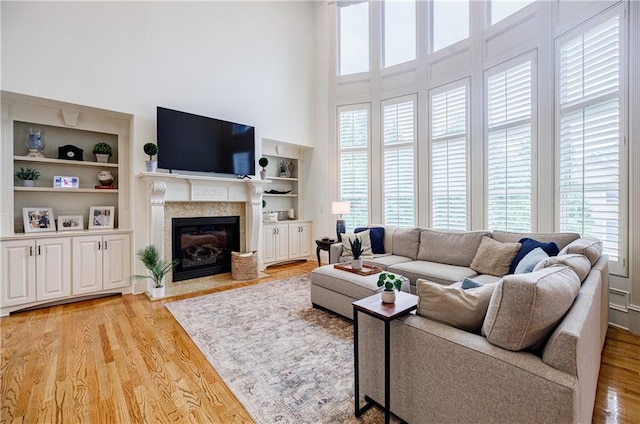 living room featuring built in shelves, light hardwood / wood-style flooring, and a high ceiling