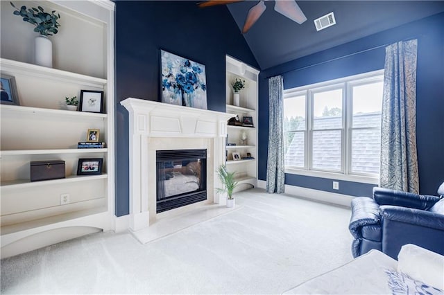 living room with built in shelves, ceiling fan, carpet floors, vaulted ceiling, and a fireplace