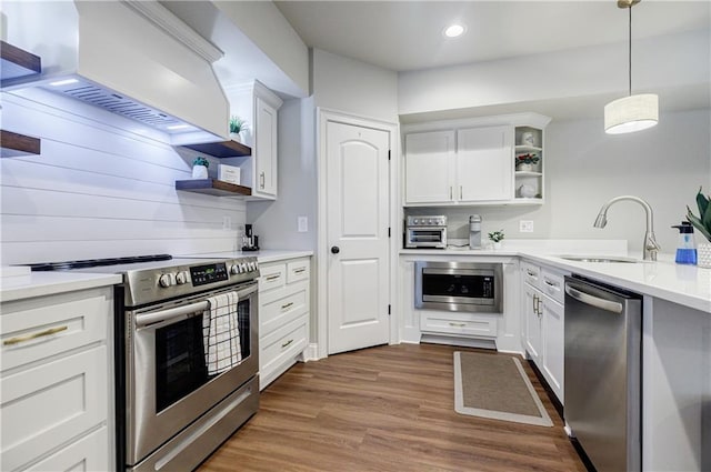 kitchen with sink, hanging light fixtures, stainless steel appliances, white cabinets, and custom range hood