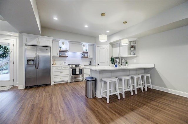 kitchen featuring a kitchen breakfast bar, kitchen peninsula, appliances with stainless steel finishes, decorative light fixtures, and white cabinetry