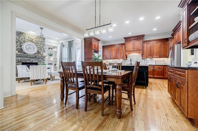 dining space featuring sink, crown molding, built in features, a fireplace, and light hardwood / wood-style floors