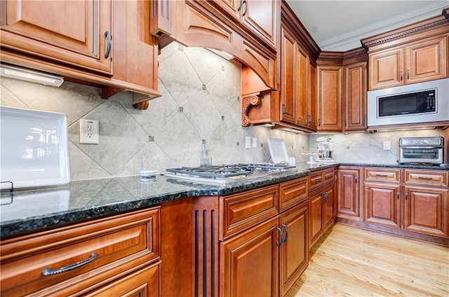 kitchen with stainless steel appliances, light hardwood / wood-style flooring, tasteful backsplash, and dark stone countertops