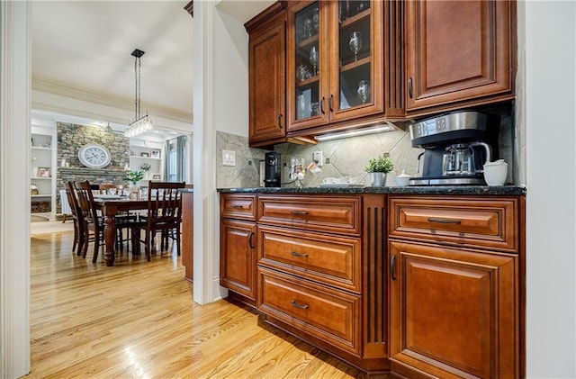 bar featuring pendant lighting, dark stone countertops, light wood-type flooring, ornamental molding, and tasteful backsplash