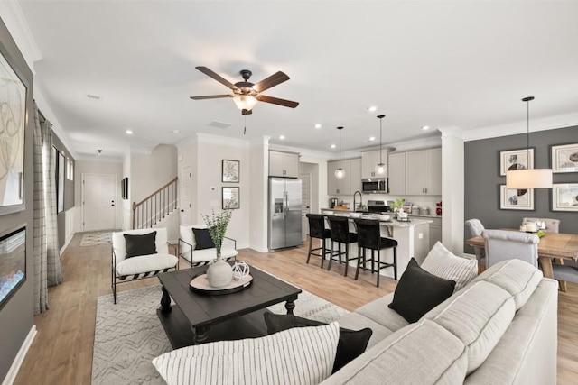 living room with ornamental molding, ceiling fan, and light wood-type flooring