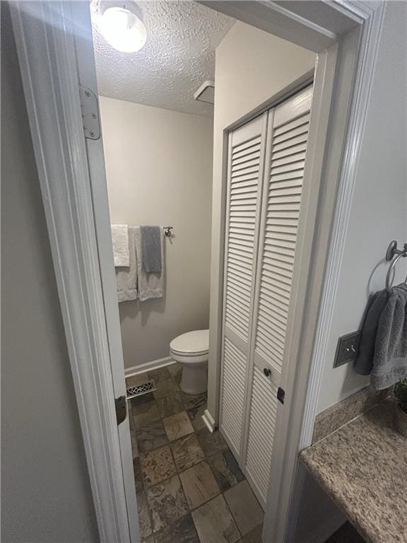 3414 Bayshore Dr, Atlanta, GA 30340 - bathroom featuring a closet, toilet, baseboards, a textured ceiling, and stone finish flooring