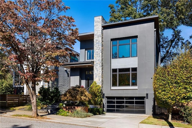 contemporary home with stucco siding, fence, concrete driveway, a garage, and a chimney