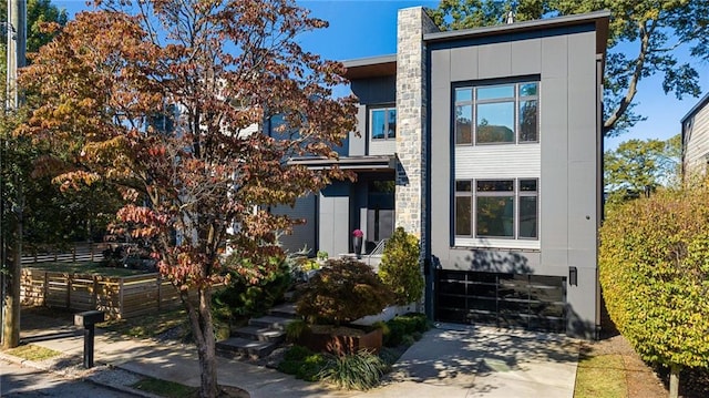 contemporary home with board and batten siding, fence, a chimney, a garage, and driveway