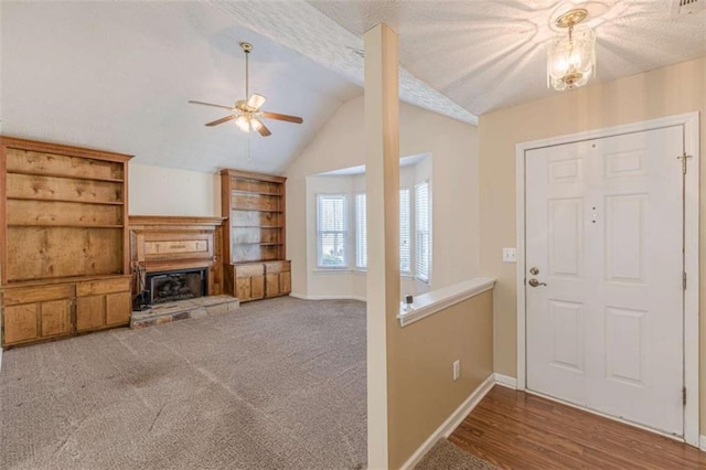 carpeted entrance foyer featuring lofted ceiling, a fireplace with raised hearth, baseboards, and a textured ceiling