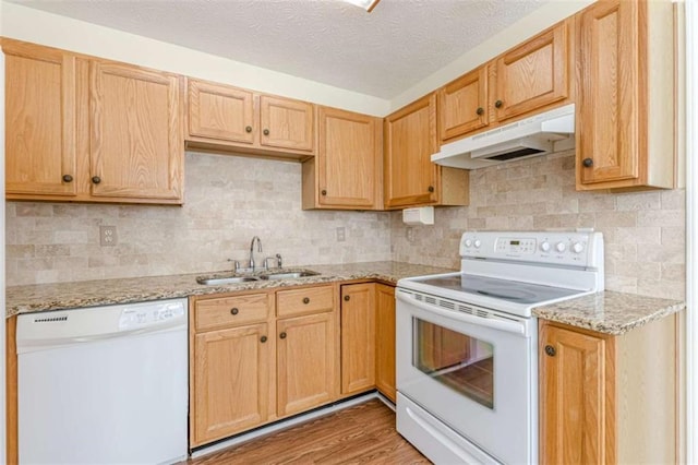 kitchen featuring light wood finished floors, light stone countertops, under cabinet range hood, white appliances, and a sink