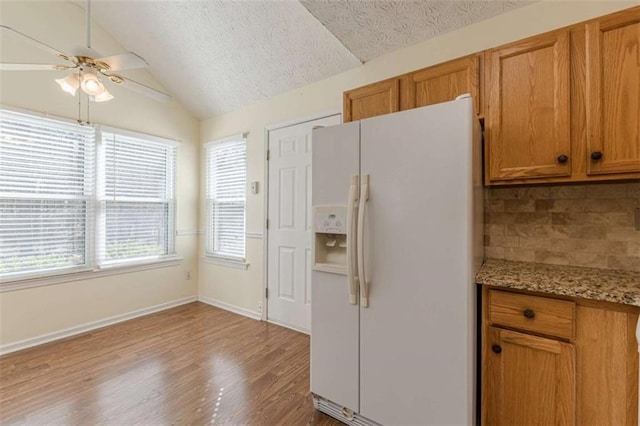 kitchen with brown cabinets, white refrigerator with ice dispenser, lofted ceiling, and wood finished floors