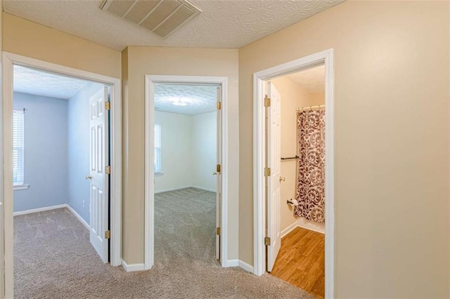 corridor with carpet, visible vents, a wealth of natural light, and a textured ceiling