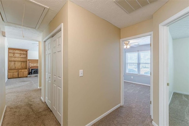 hallway featuring baseboards, visible vents, attic access, a textured ceiling, and carpet flooring